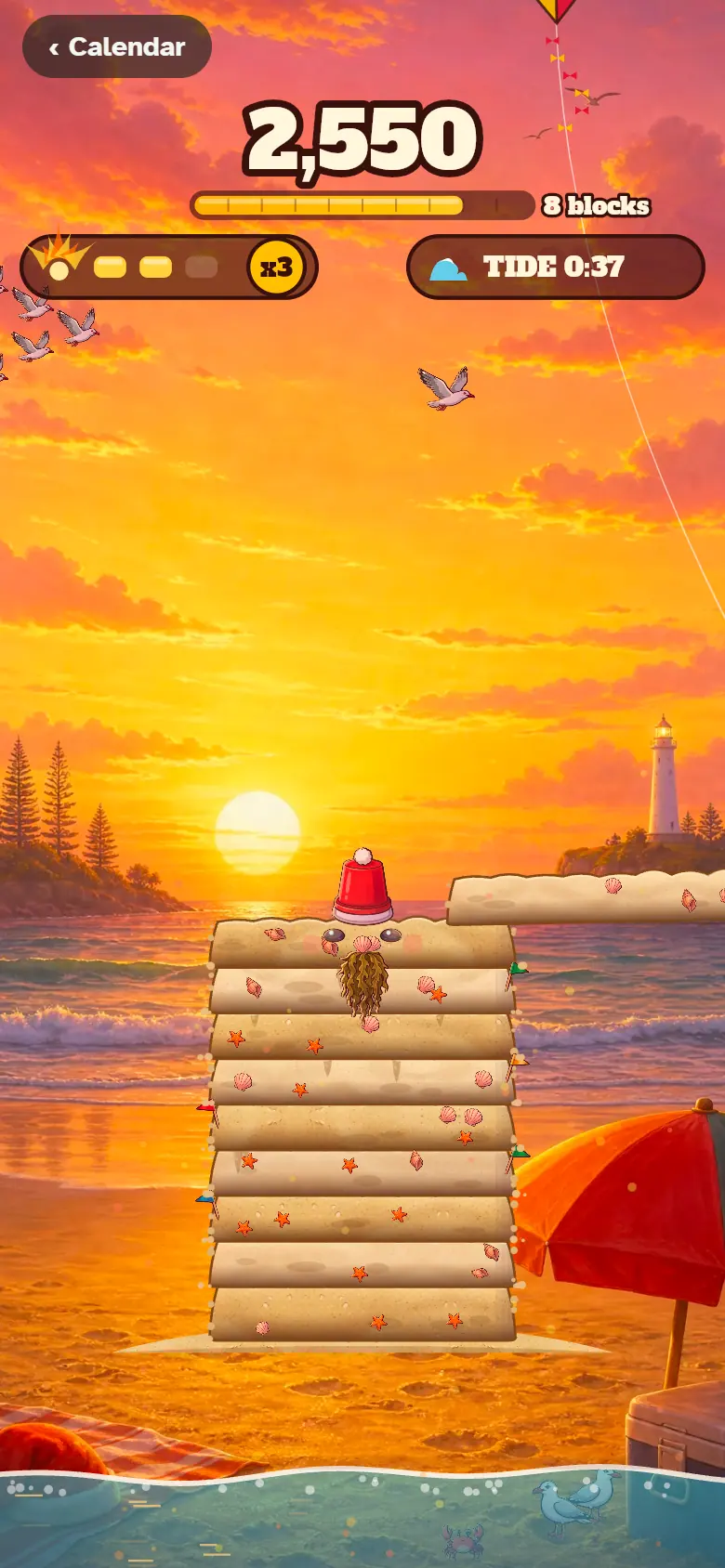 A tall Sandy Claus sculpture of stacked sand blocks rises on the beach at sunset before the tide comes in.